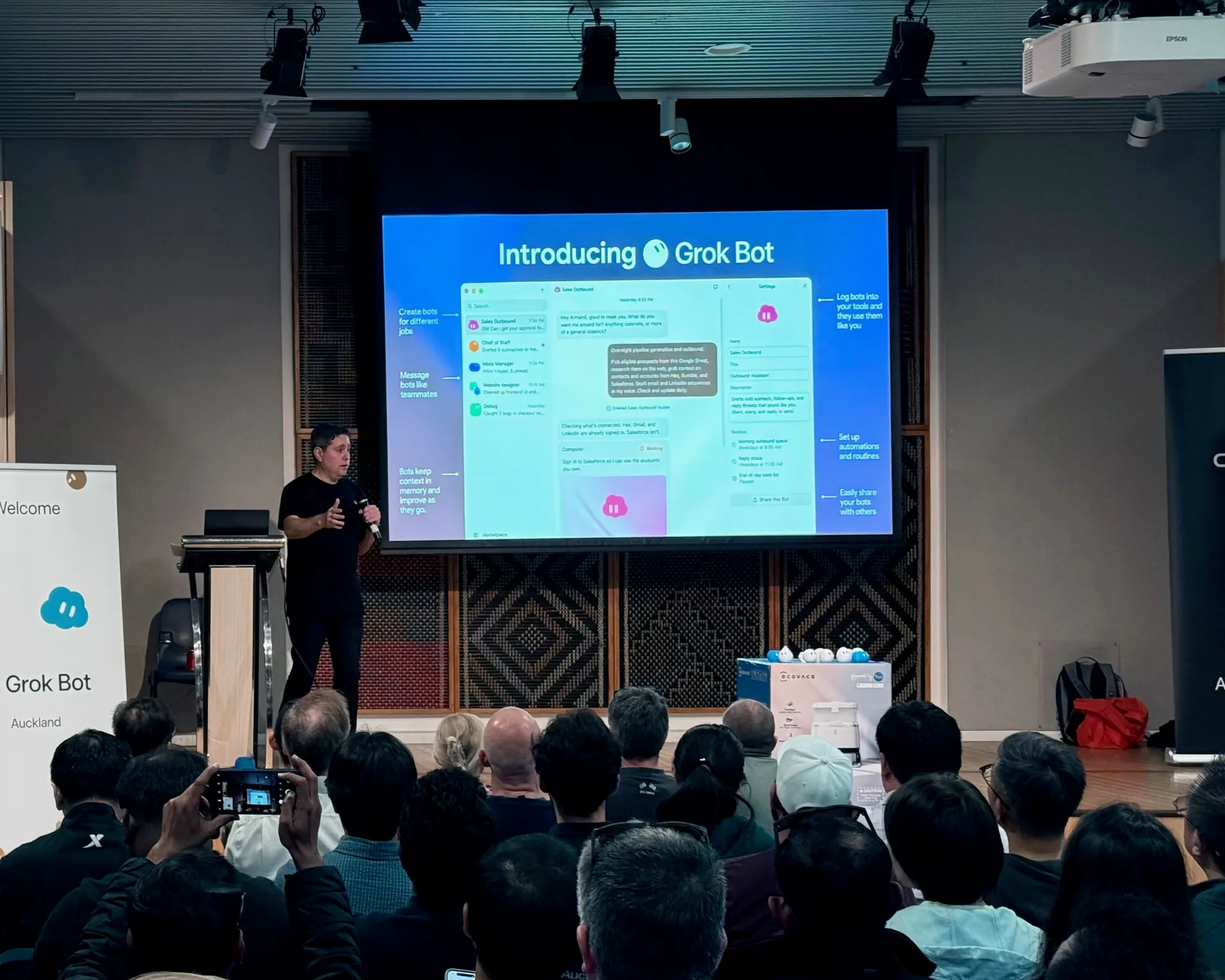 Presenter beside the Introducing Grok Bot slide as an attendee photographs the stage