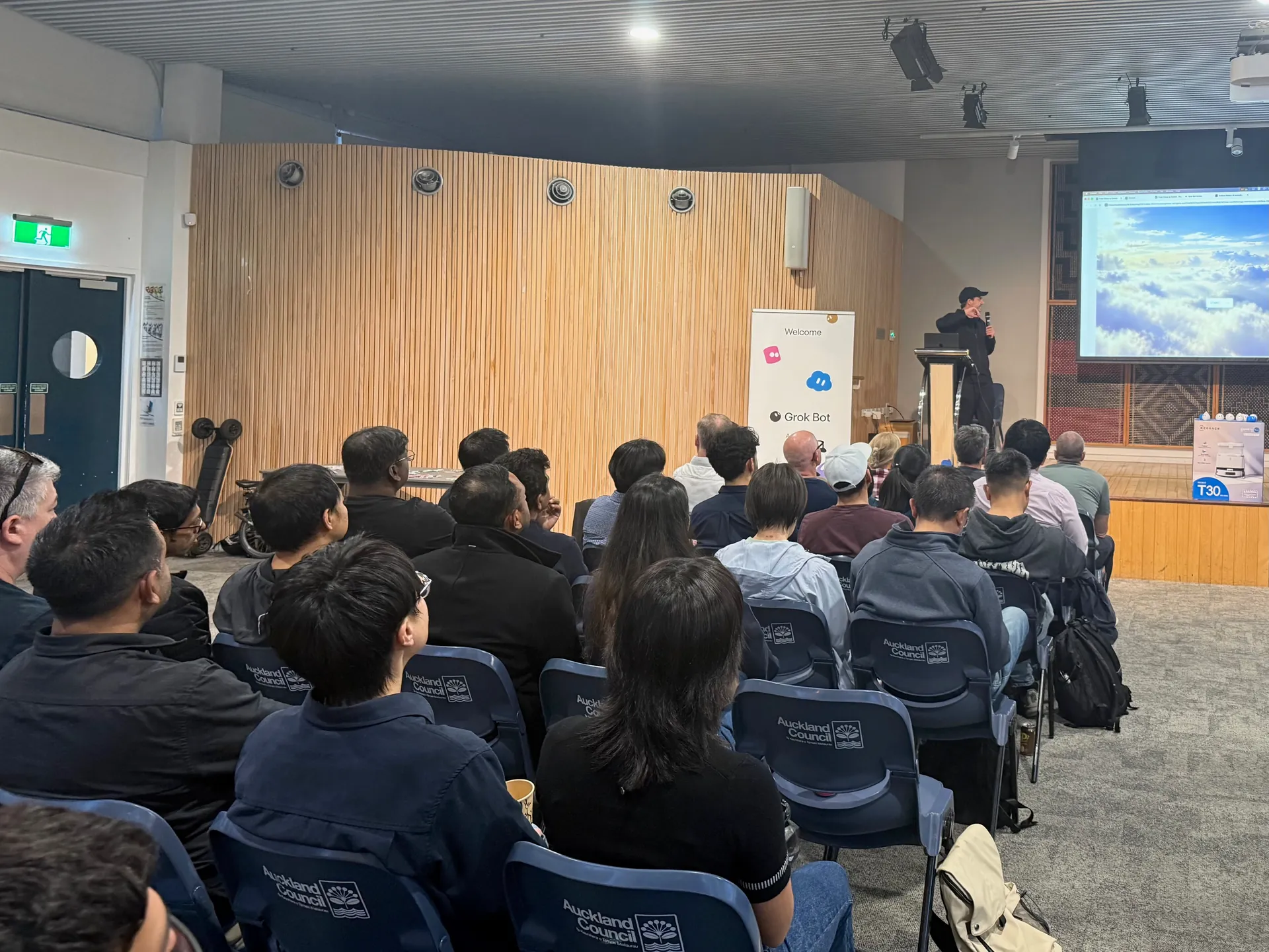 Speaker in a cap presenting at the lectern to a full hall