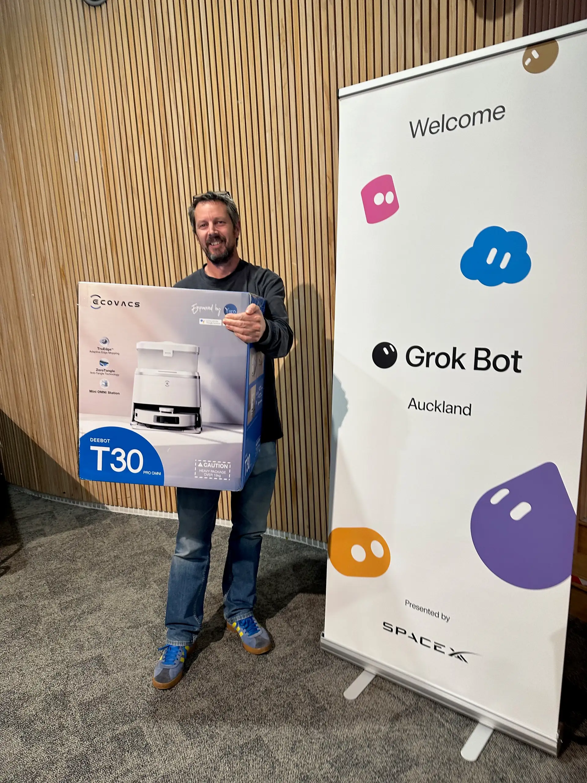 Kahoot winner holding the robot vacuum prize next to the Grok Bot Auckland banner