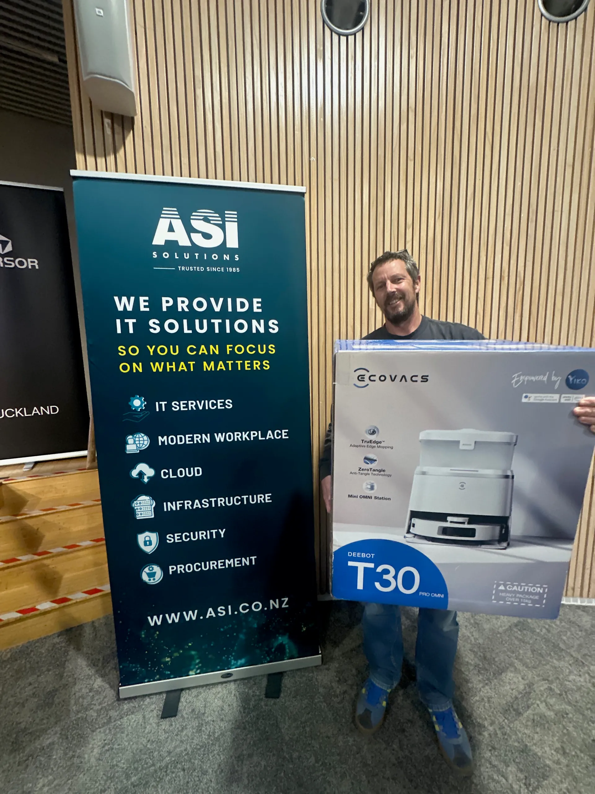 Kahoot winner with the robot vacuum prize in front of the ASI Solutions banner