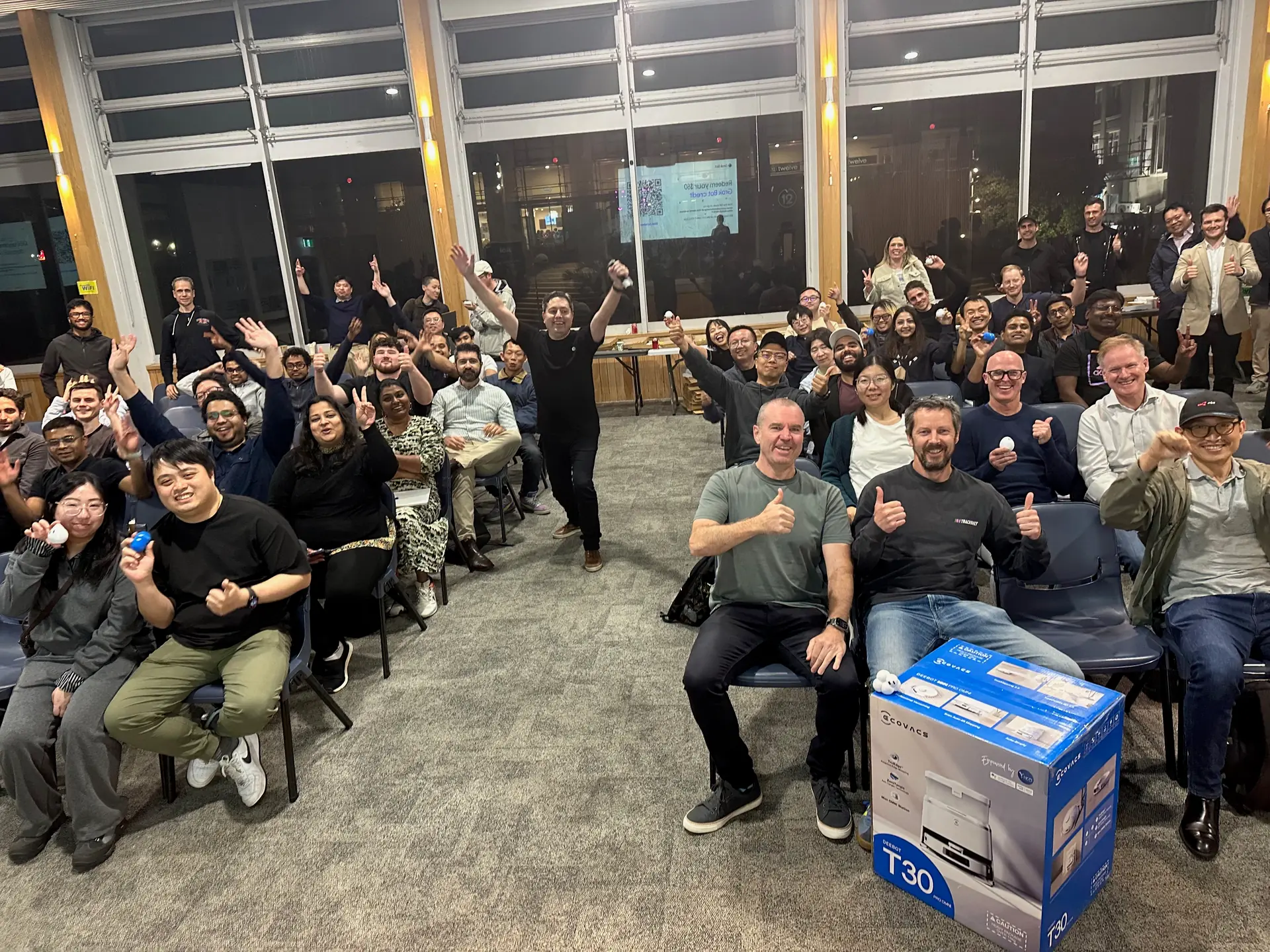 Group photo of attendees giving a thumbs up, with the vacuum prize box in front