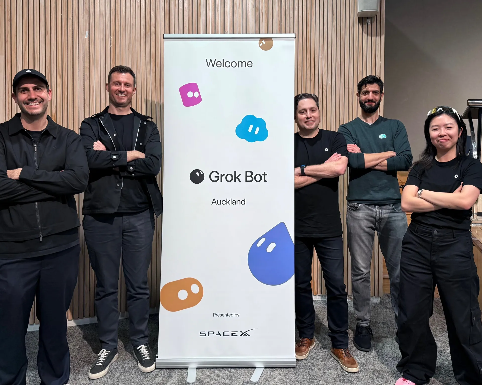 Team photo with arms crossed beside the Grok Bot Auckland banner